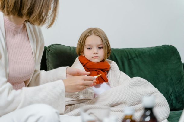 doctor checking the temperature of her child patient while sitting on green couch