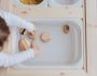 unrecognizable kid playing with stones in white container at table at home