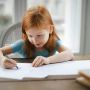 diligent small girl drawing on paper in light living room at home